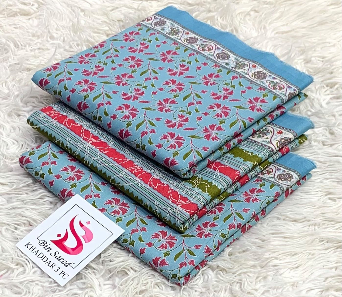 Folded light blue Bin Saeed khaddar 3 piece unstitched suit with pink floral patterns.